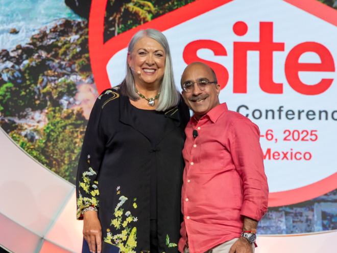 two individuals pose onstage, facing the camera and smiling